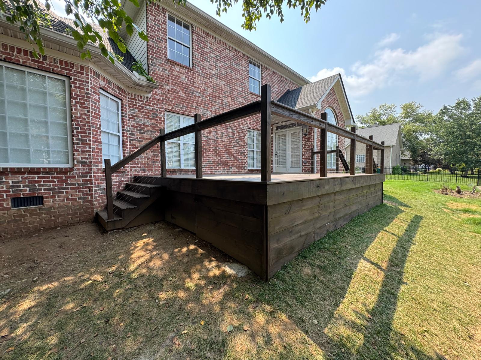 Wood deck with cable railing, enclosed sides and steps beside a brick home